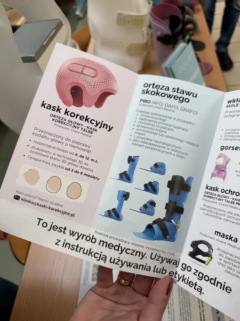 Ulotka reklamowa przedstawiająca różne wyroby medyczne. Po lewej stronie znajduje się informacja o "kasku korekcyjnym" przeznaczonym do poprawy kształtu głowy u niemowląt. Kask jest różowy i ma otwory wentylacyjne. Podano, że terapia trwa od 2 do 6 miesięcy. Po prawej stronie ulotki znajduje się informacja o "ortezie stawu skokowego" o nazwie PIRO, która znajduje zastosowanie w przypadku chodu krzyżowego, nadmiernej pronacji i innych problemów. Na dole ulotki znajduje się ostrzeżenie, że jest to wyrób medyczny i należy go używać zgodnie z instrukcją. W tle widać różne medyczne urządzenia i osoby stojące przy stole.