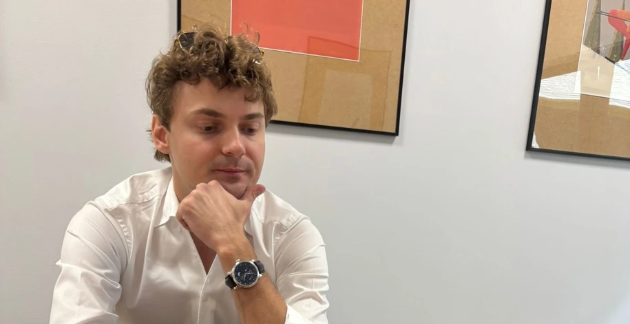 Mężczyzna w białej koszuli siedzi przy stole, na którym rozłożone są certyfikaty