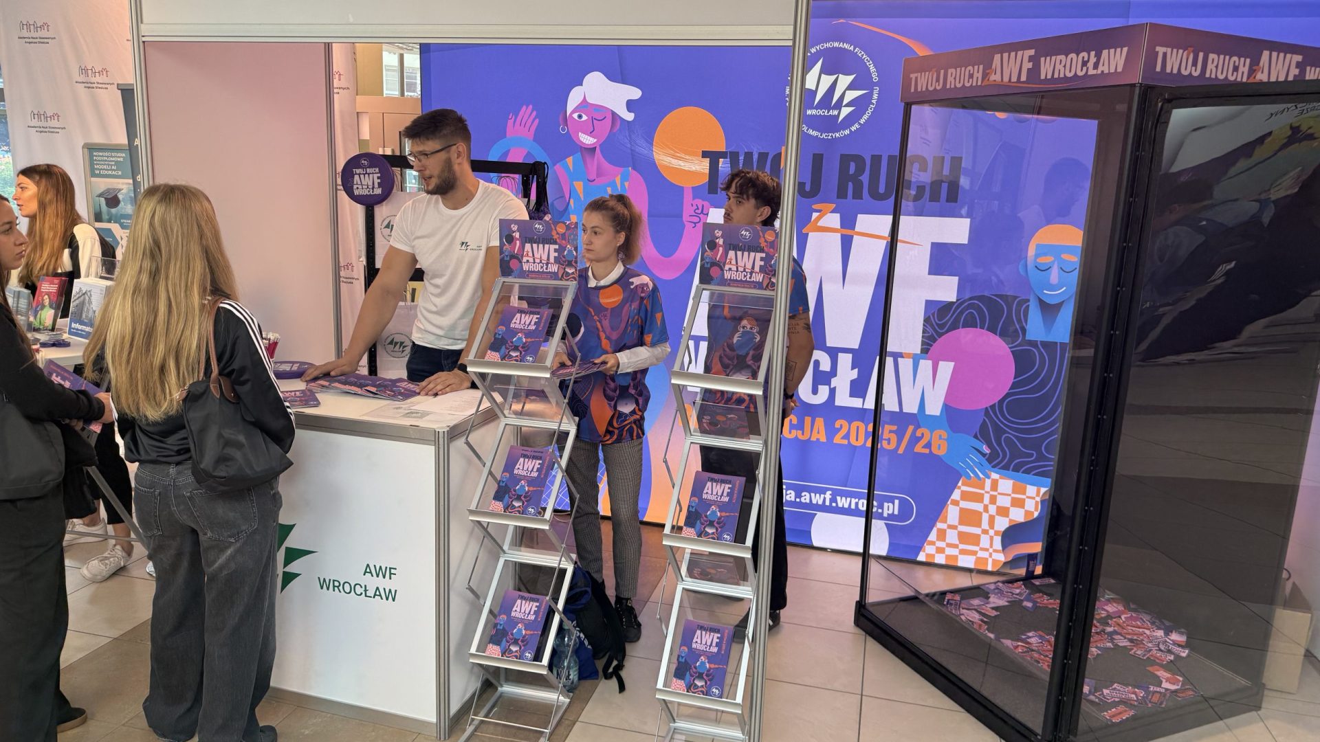 Ludzie na stoisku promocyjnym AWF kolory ścianek fiolet, róż
