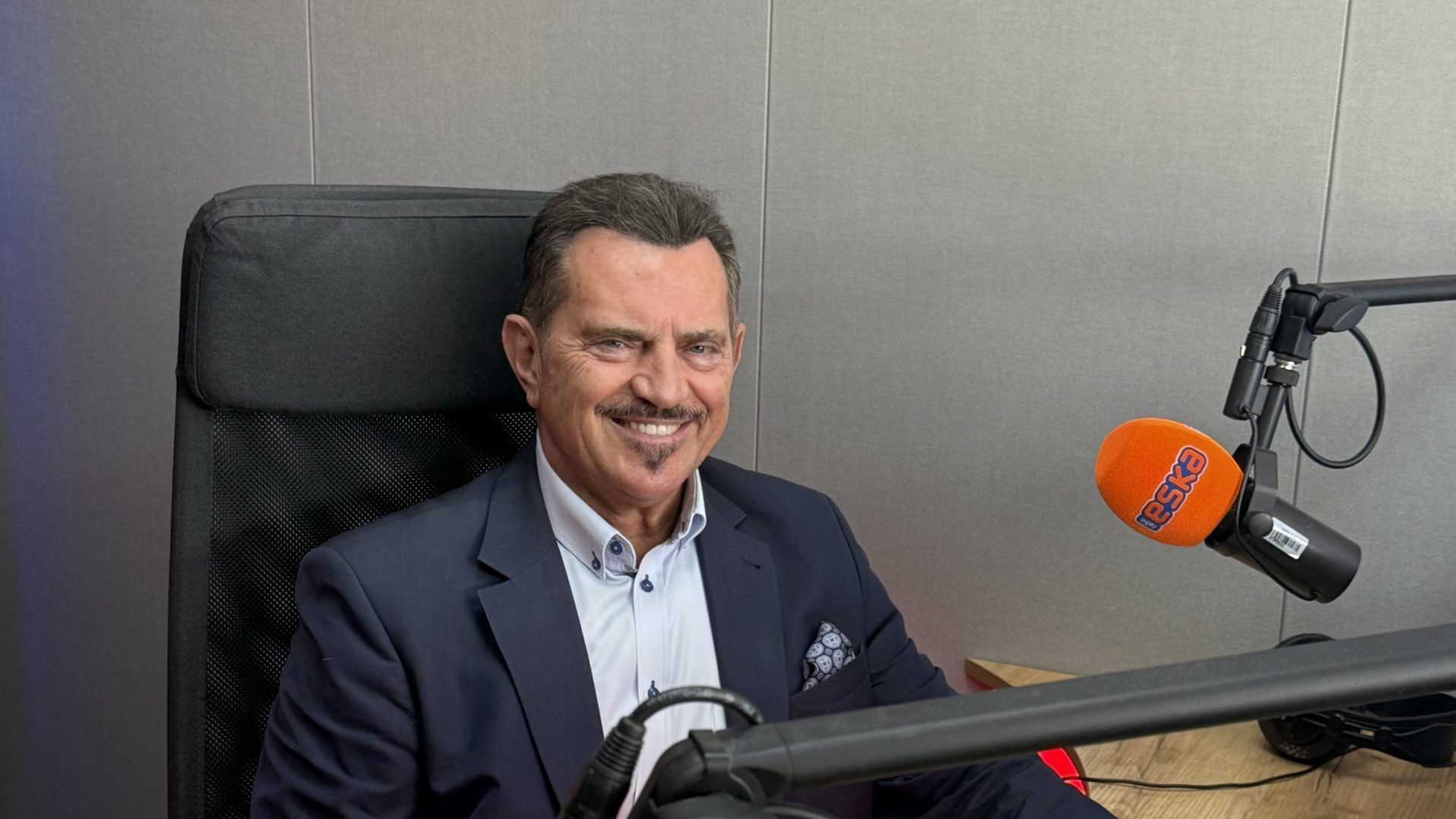 mężczyzna w studiu radiowym, pomarańczowe mikrofony, szare ściany