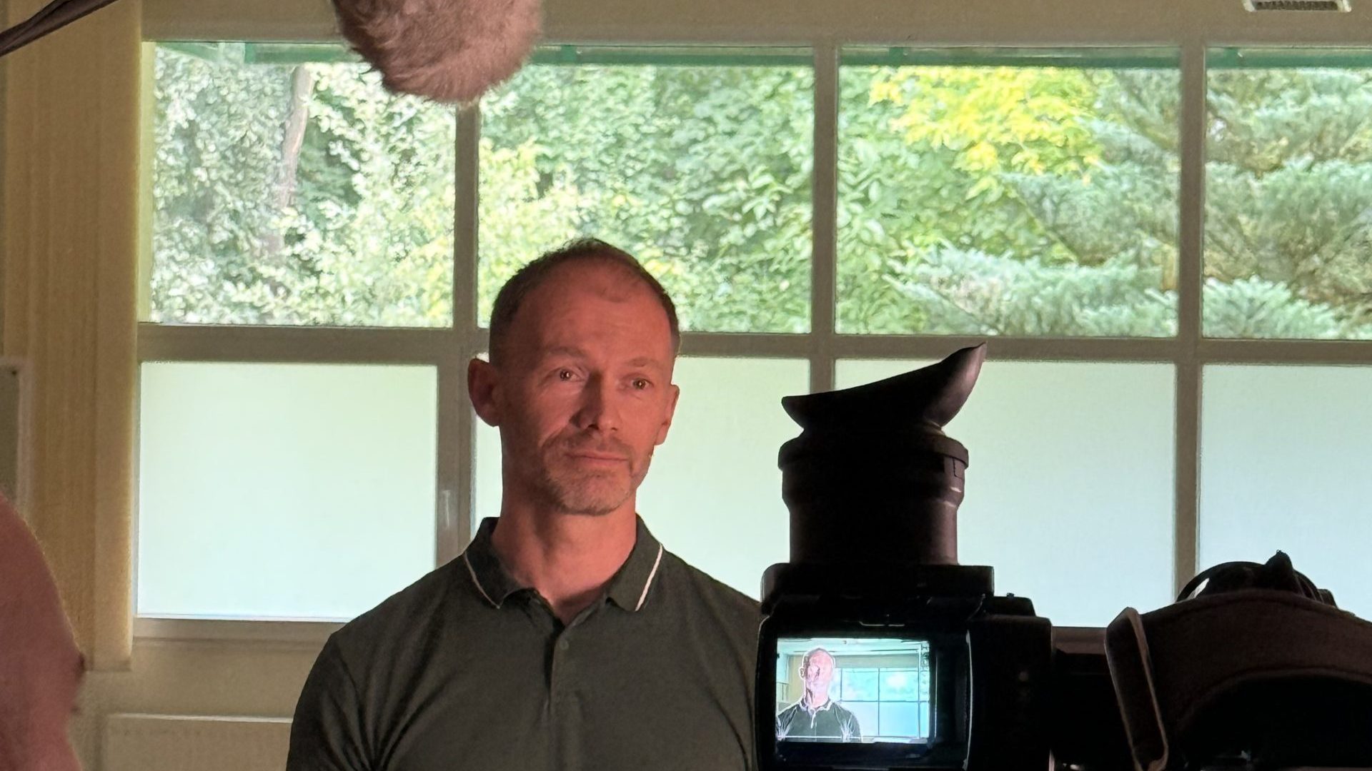 mężczyzna w zielonym polo na sali gimnastycznej z góry wisi mikrofon telewizyjny, mężczyzna stoi przed kamerą