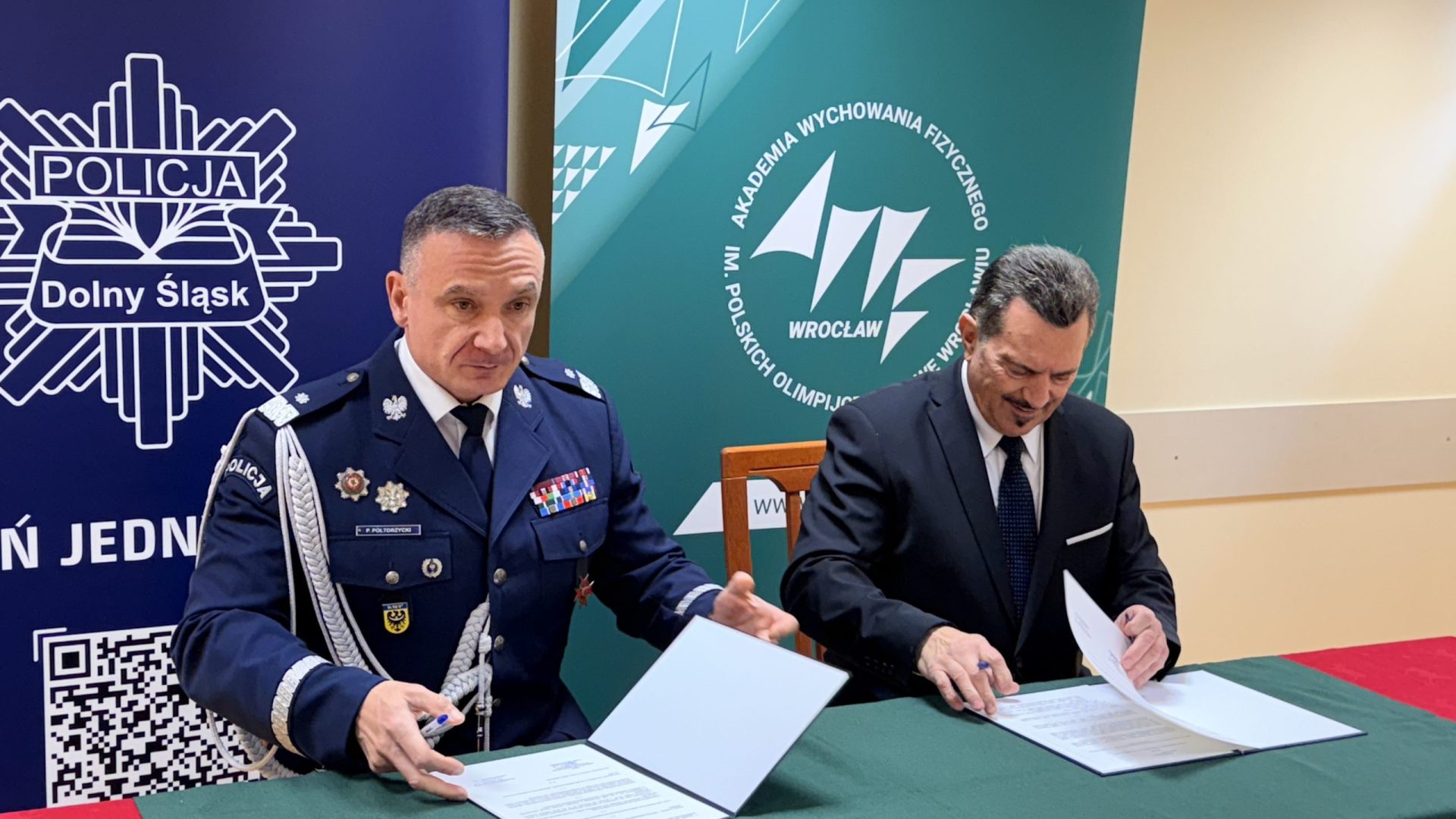 dwaj mężczyźni przy stole podpisują umowę, jeden w mundurze, drugi w garniturze.