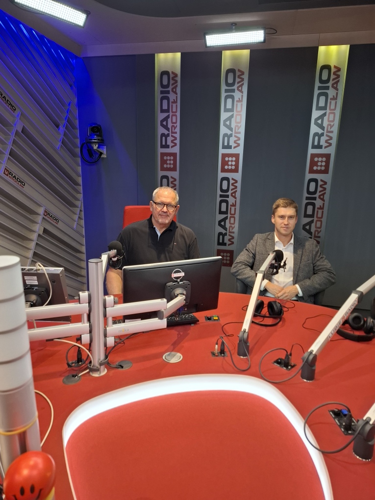 Dwaj mężczyźni w studiu radiowym, stół i kilka mikrofonów