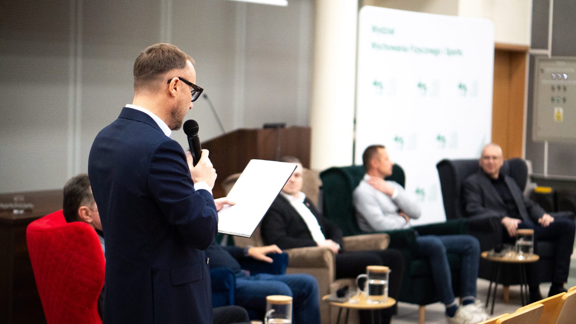 mężczyźni siedzą na fotelach w sali wykładowej