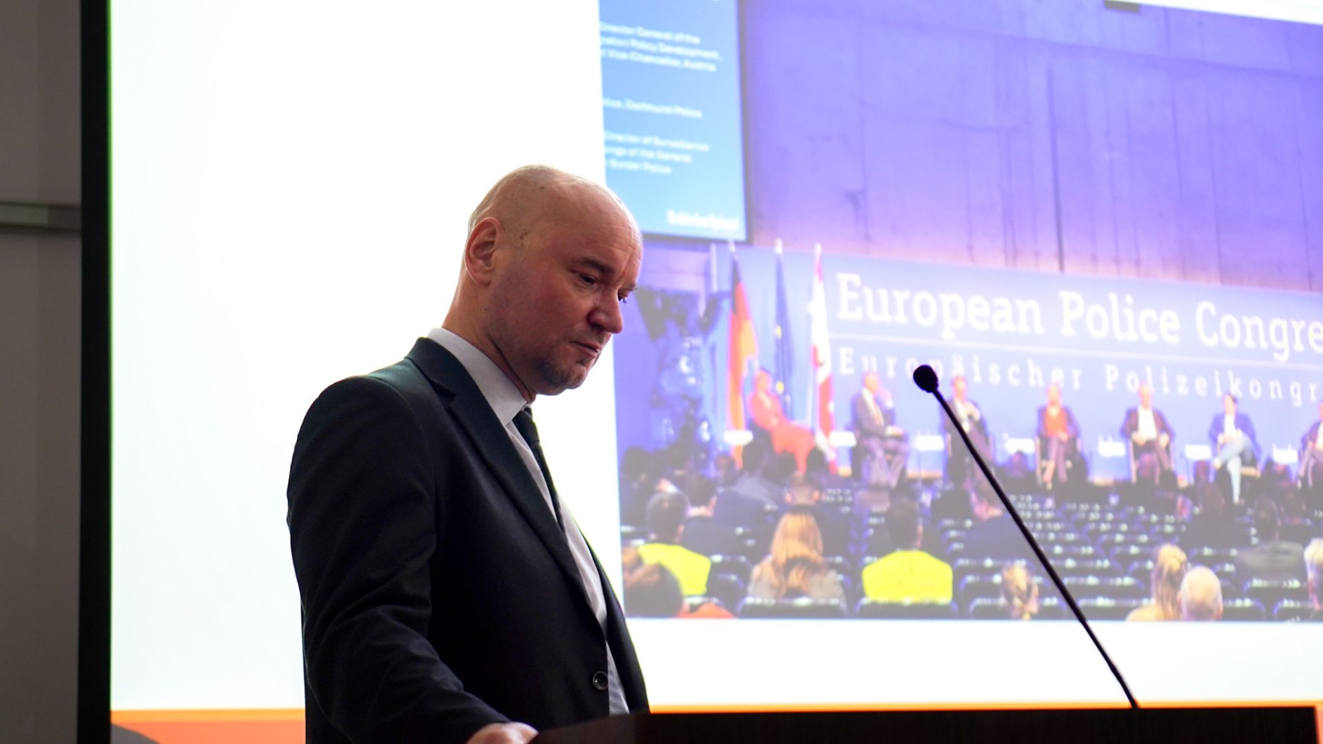 mężczyzna w garniturze na tle ekranu