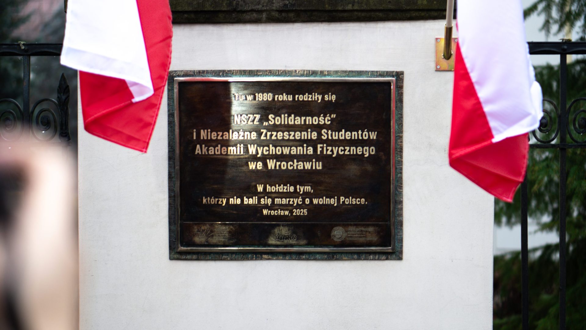 tablica i dwie polskie flagi