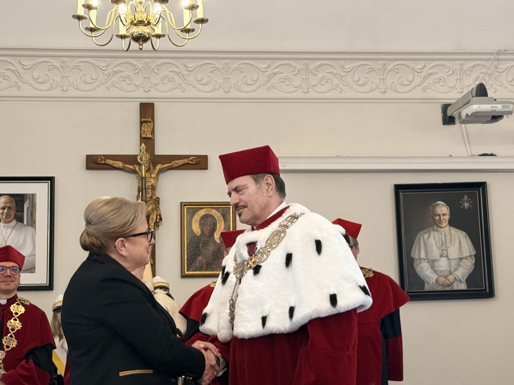Rektor w todze odbiera odznaczenie od kobiety