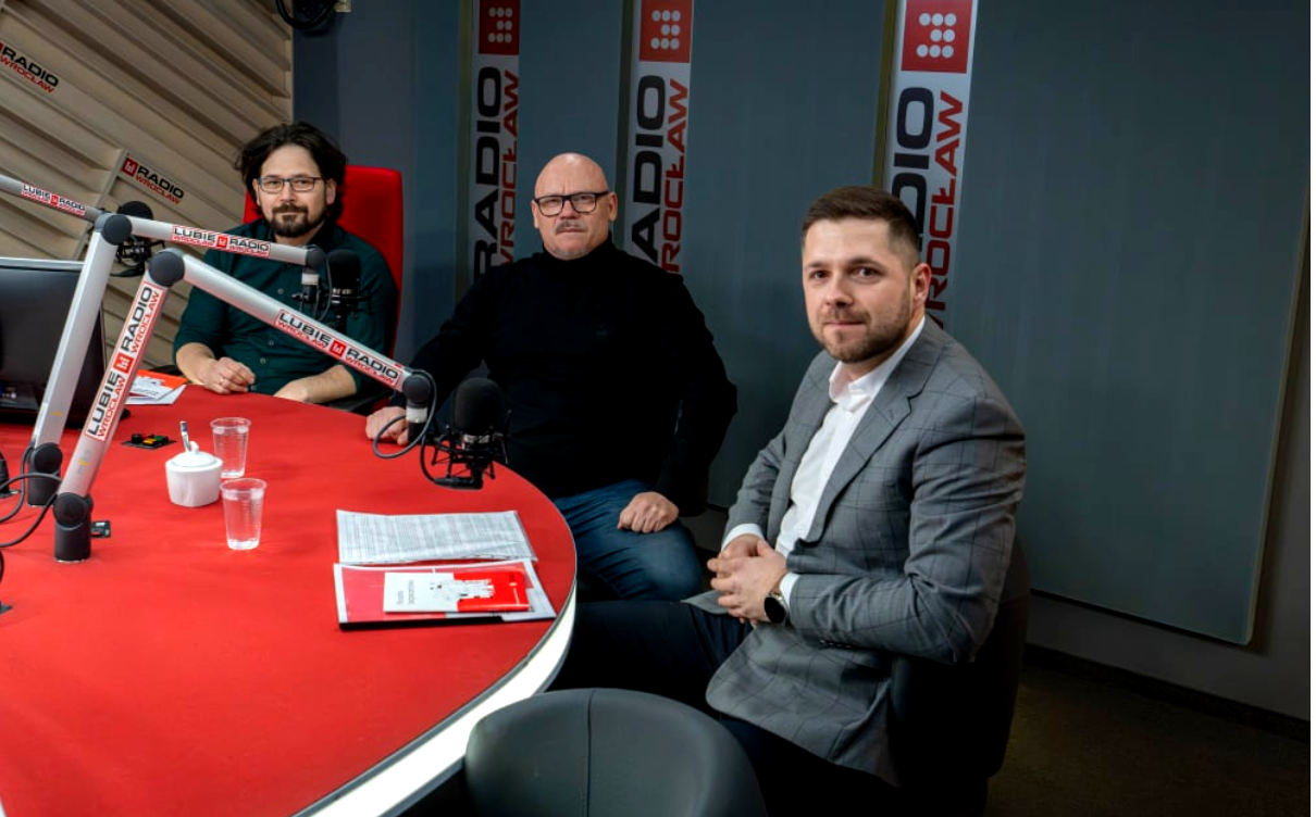 trzech mężczyzn przy czerwonym stoliku z mikrofonami, studio radiowe