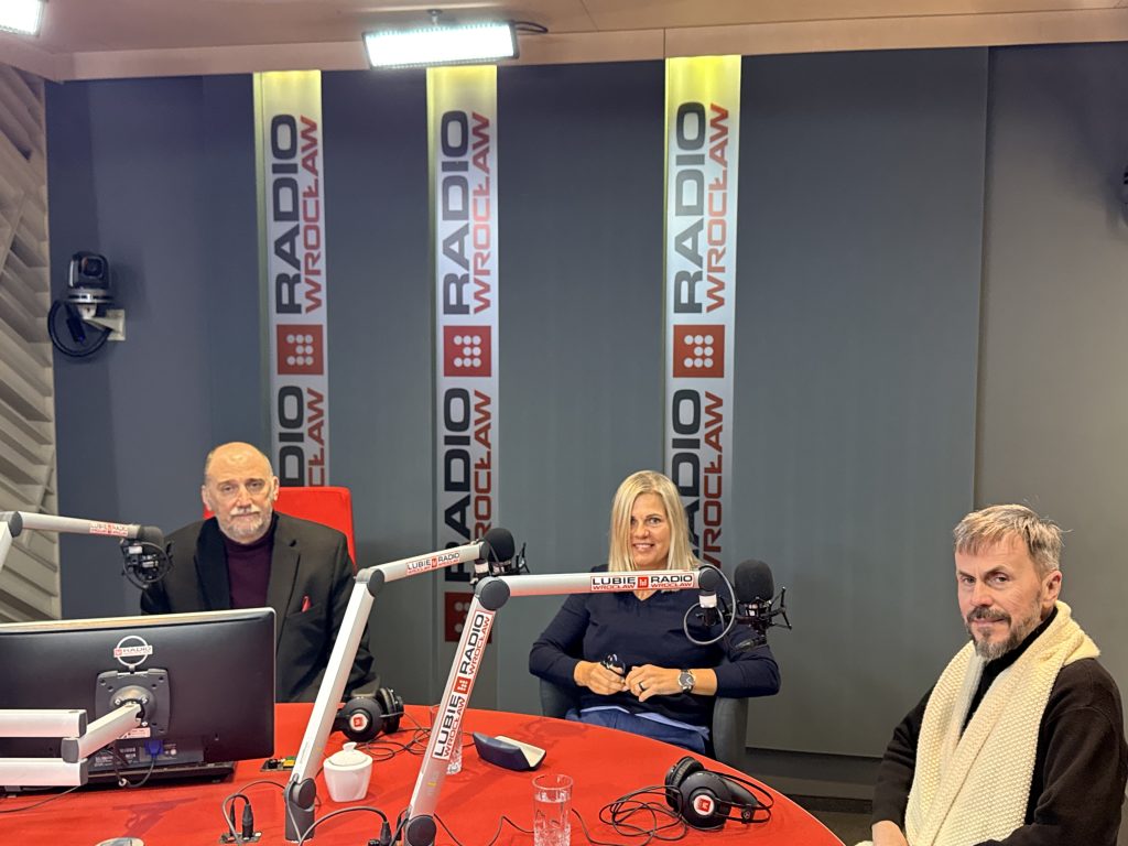 kobieta i dwóch mężczyzn w studiu radiowym przy stole, przed mikrofonami