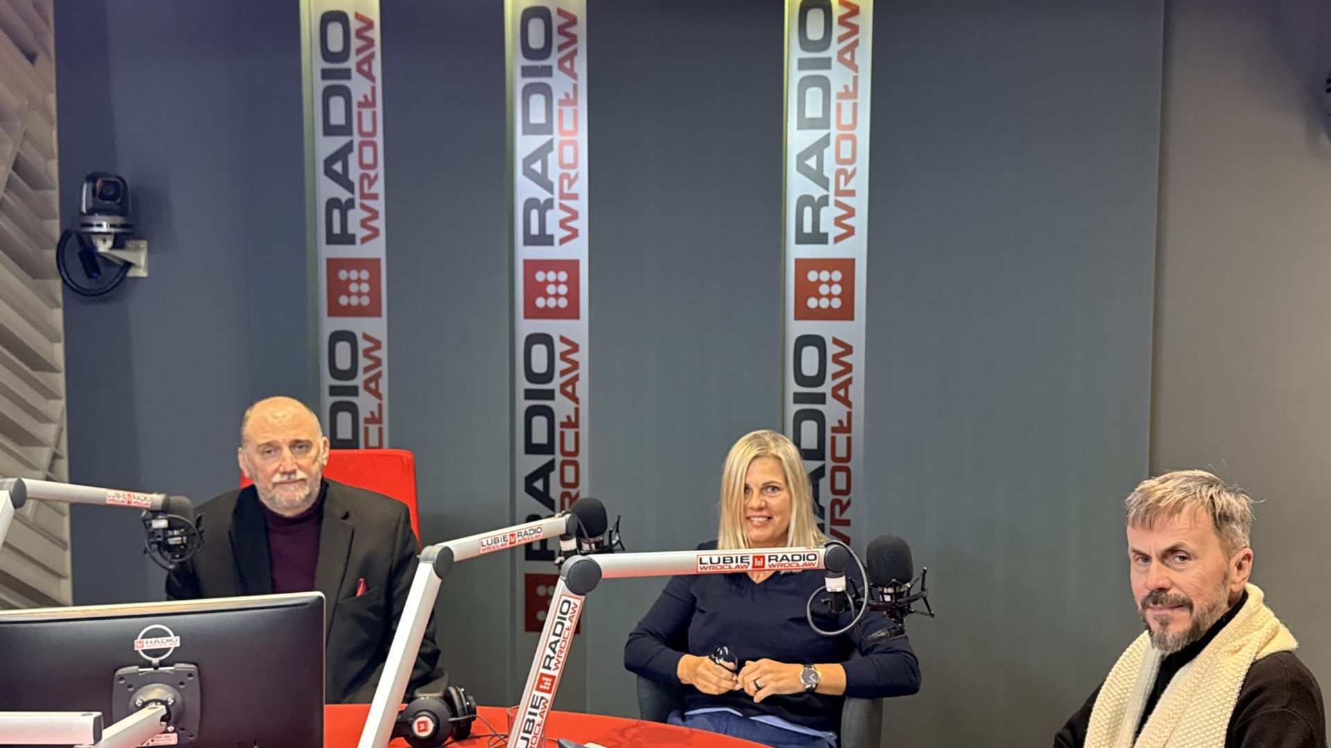 kobieta i dwóch mężczyzn w studiu radiowym przy stole, przed mikrofonami