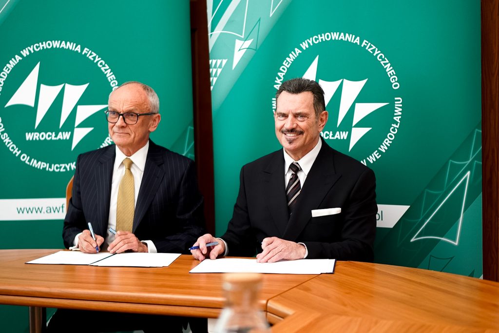 dwaj mężczyźni podpisują umowę na tle zielonych rollupów reklamowych