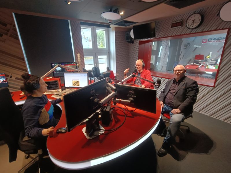 studio radiowe, stół z mikrofonami, troje ludzi